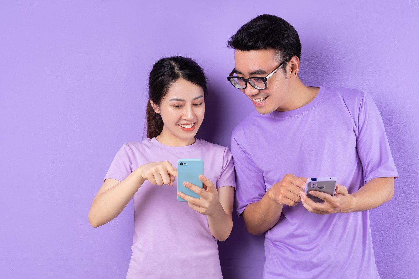 Young Asian Couple Using Smartphone on Purple Background